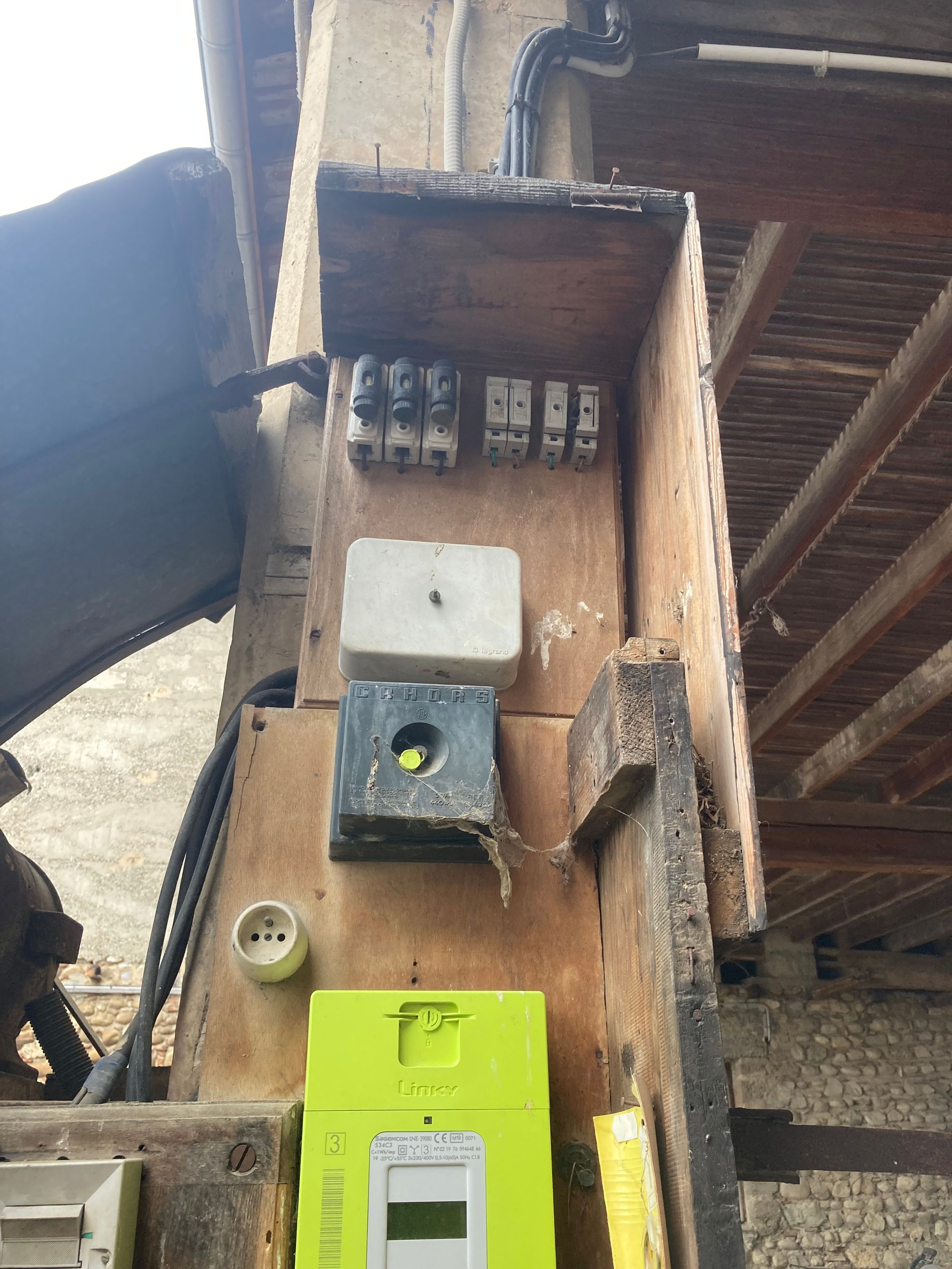 Gros plan sur un poteau électrique avec des boîtes électriques et des câbles sous un avant-toit.