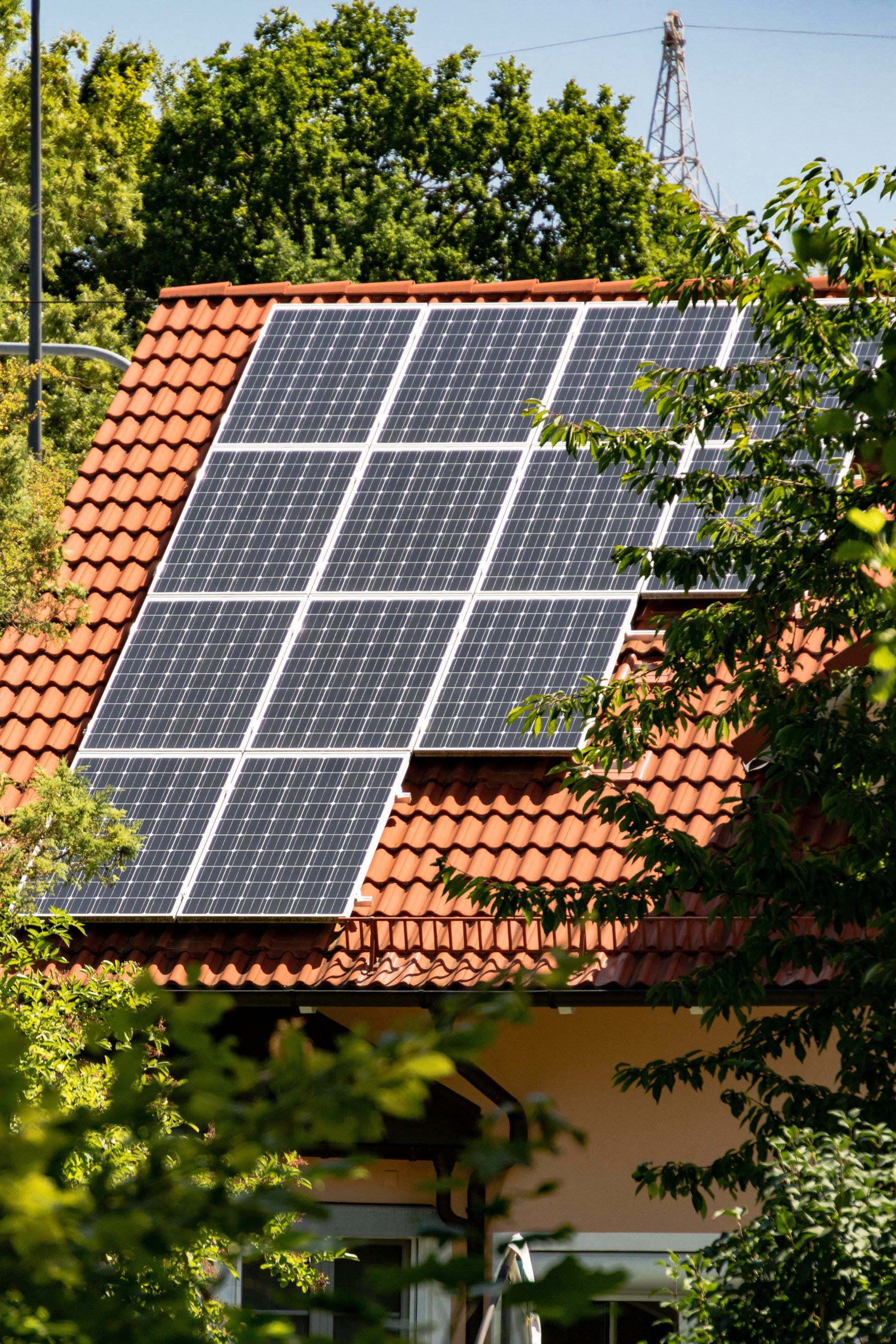 Des panneaux solaires installés sur un toit de tuiles, au milieu d'arbres verdoyants.