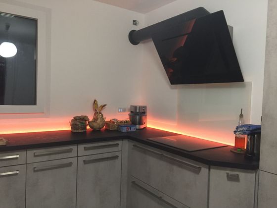 Coin cuisine moderne avec placards, plan de travail, éclairage LED et hotte murale.