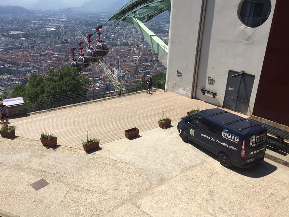 Terrasse de la station de téléphérique surplombant la ville, avec une camionnette garée à côté de plantes en pot.