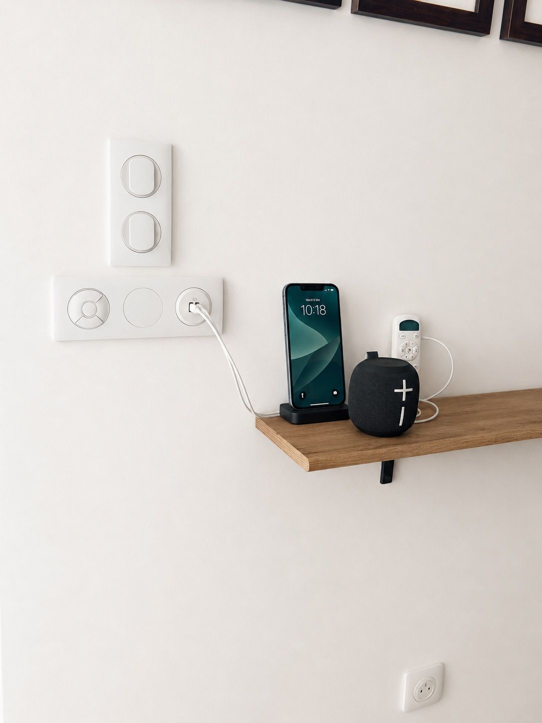 Mur avec prises électriques, étagère sur laquelle reposent un téléphone, un haut-parleur, une bouteille et un câble de chargement.