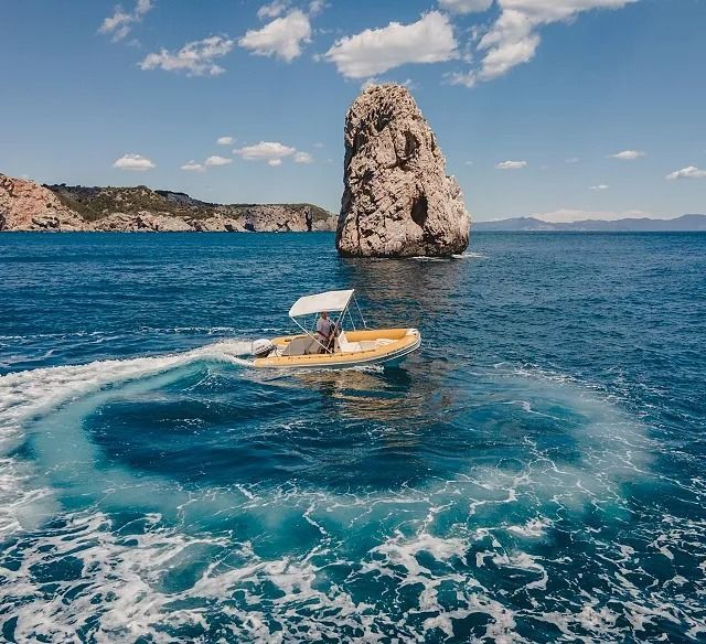 Un barco flota en el océano con una gran roca en el fondo.