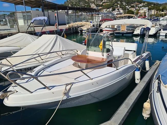 Un barco blanco está atracado en un puerto deportivo junto a otros barcos.