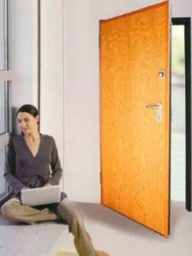 Una mujer está sentada en el suelo con una computadora portátil frente a una puerta abierta.