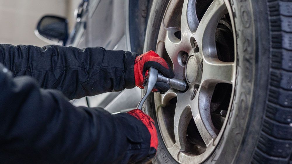 Eine Person wechselt mit einem Schraubenschlüssel einen Reifen an einem Auto.