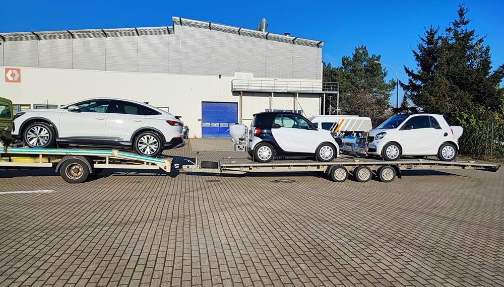 Ein Abschleppwagen transportiert drei Autos auf einem Parkplatz.