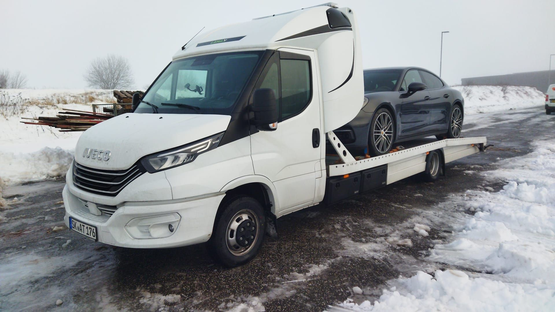 Ein weißer Abschleppwagen transportiert ein schwarzes Auto auf einer verschneiten Straße.