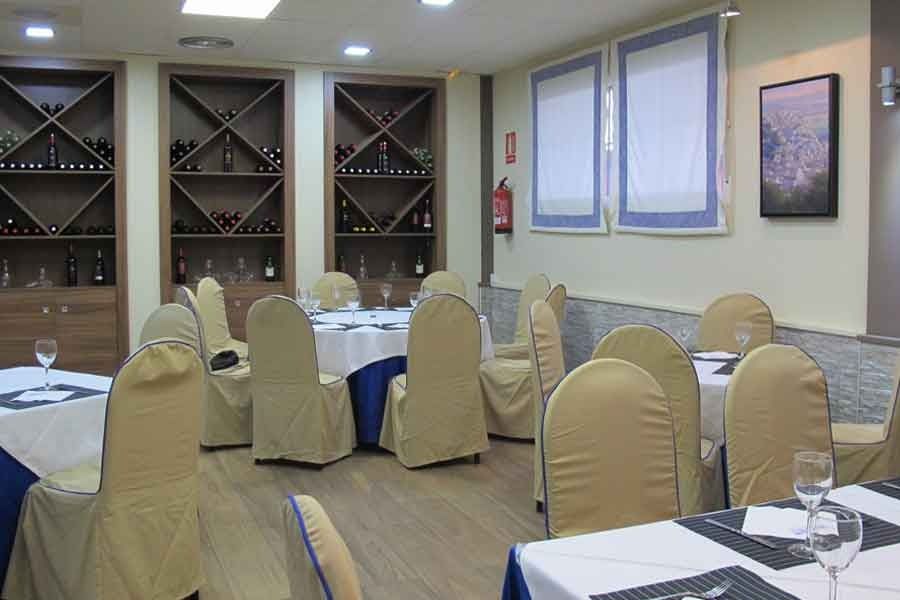 Un comedor con mesas y sillas preparadas para una comida.