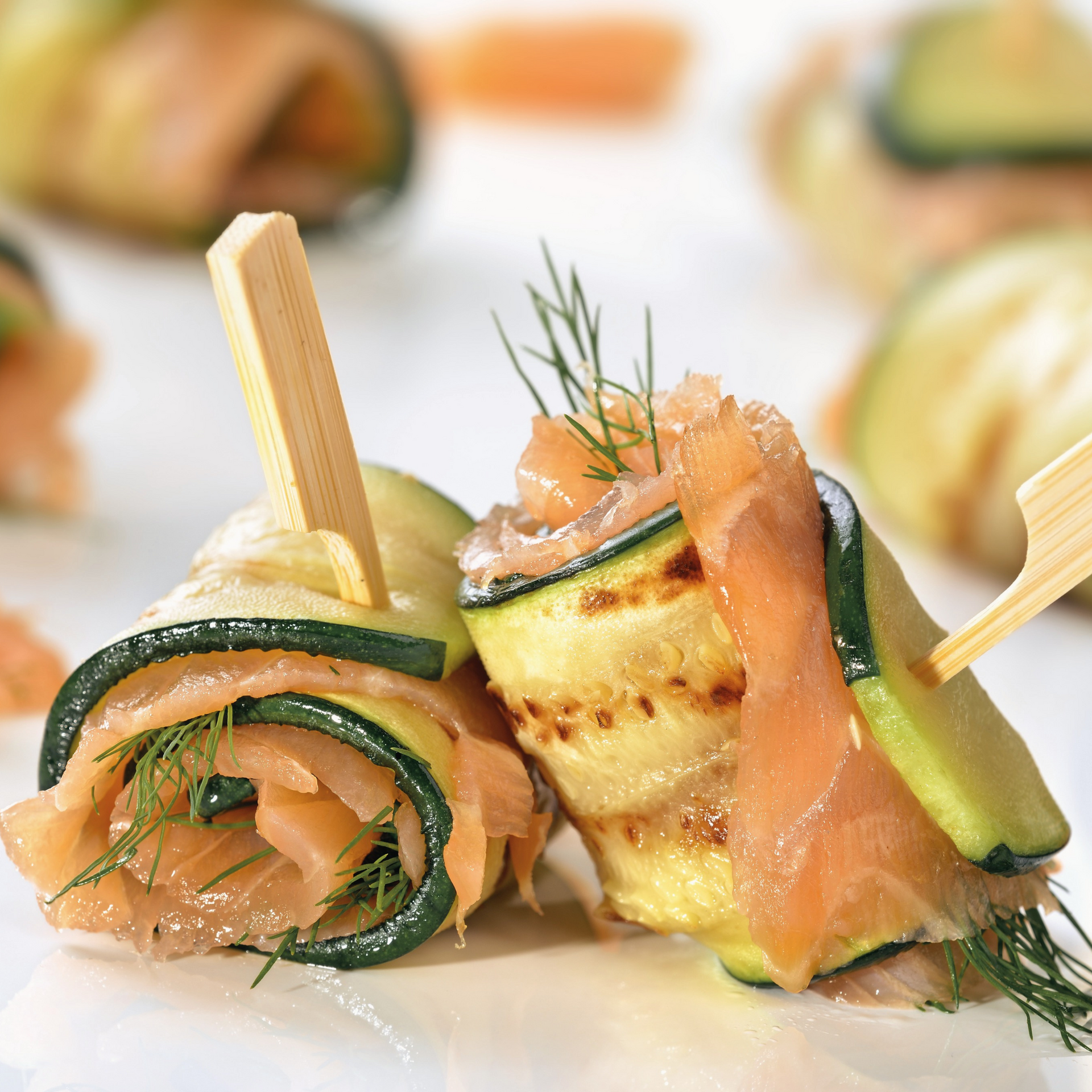 Un primer plano de un rollo de salmón ahumado y calabacín en un palillo.