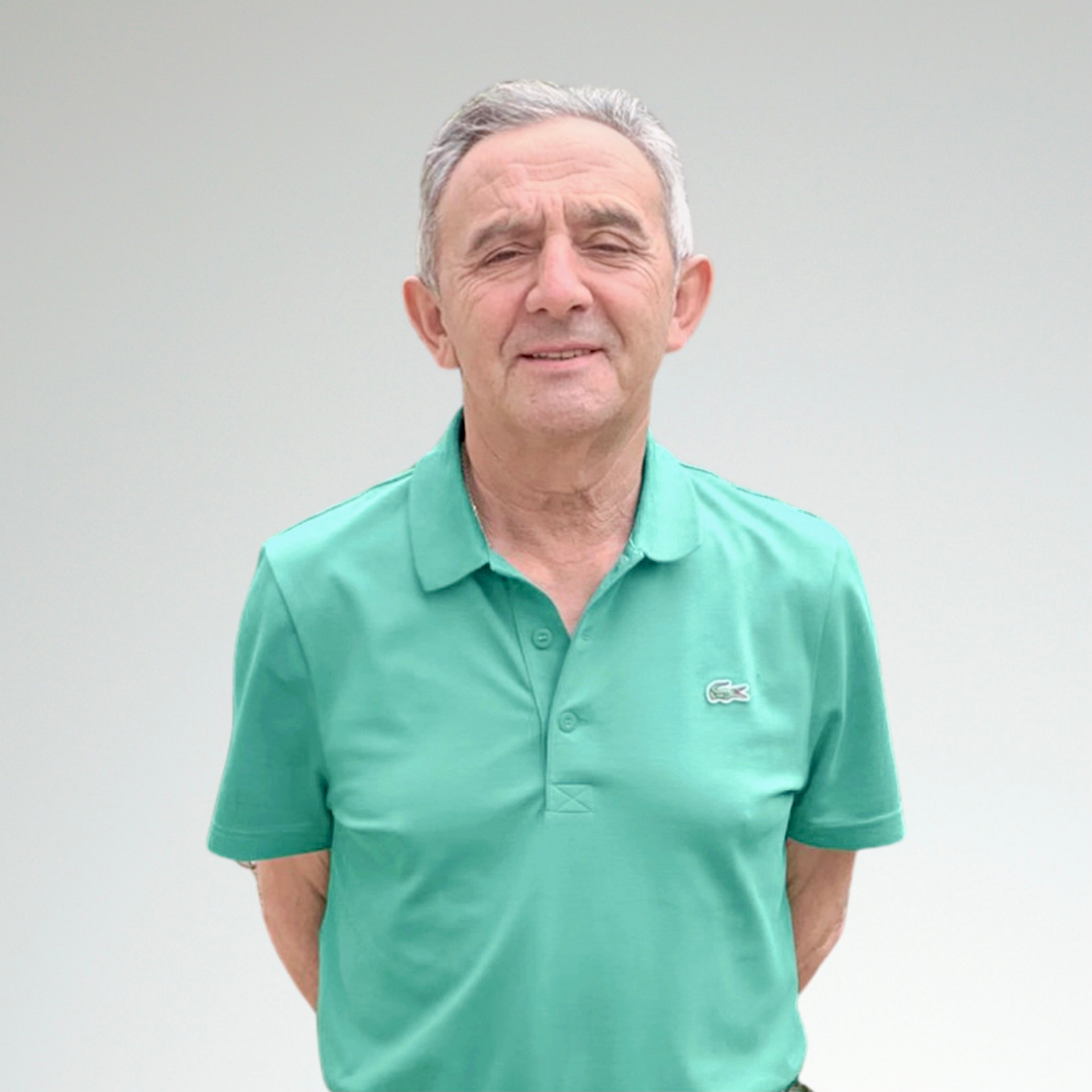 Un hombre con un polo verde está de pie con las manos detrás de la espalda.