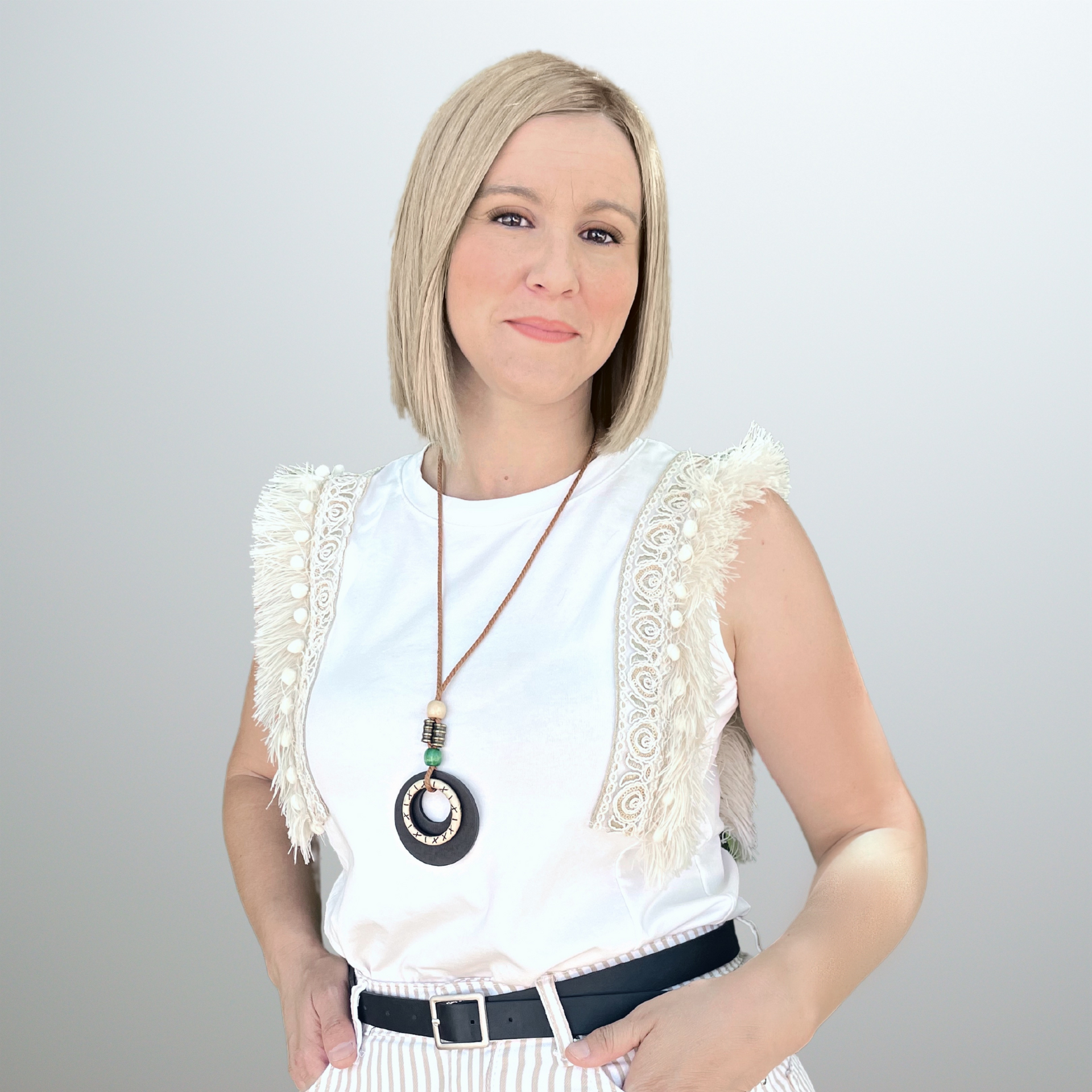 Una mujer que lleva una camisa blanca y un collar está de pie con las manos en los bolsillos.