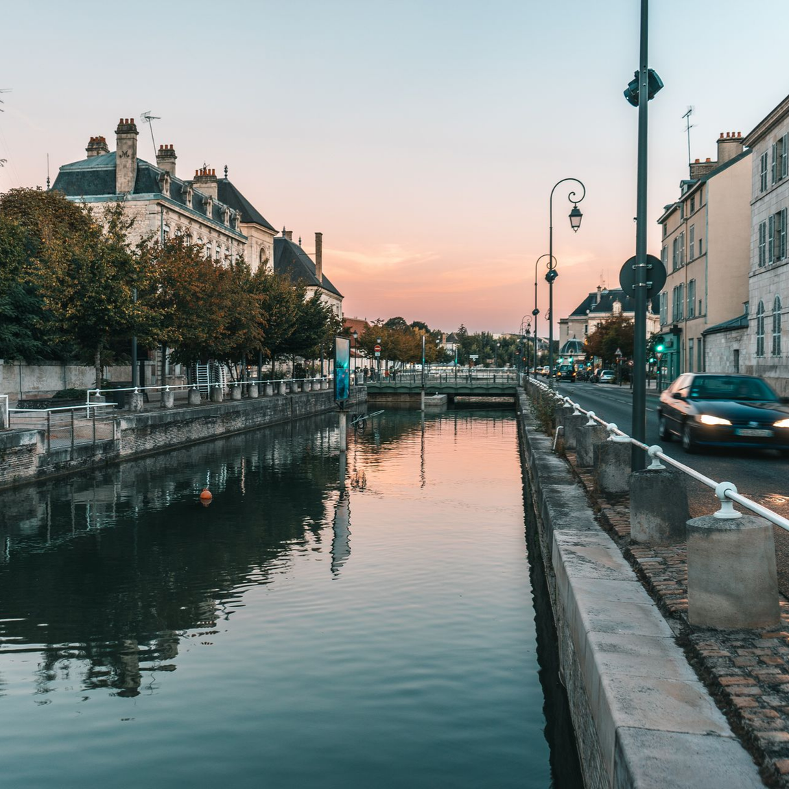 Canal dans la ville de Troyes. L'eau et le ciel rose, des bâtiments bordant le canal, une voiture à droite.