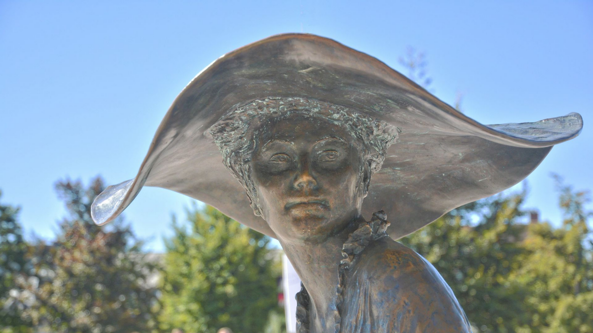Statue en bronze d'une femme avec un chapeau à larges bords, en extérieur.