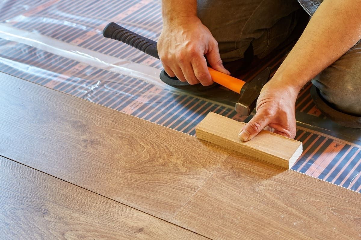Una persona está colocando un piso de madera con un martillo.