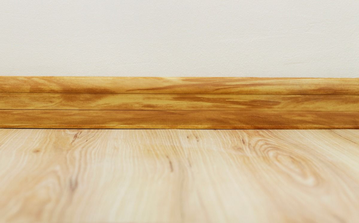 Un suelo de madera con rodapié de madera y una pared blanca.