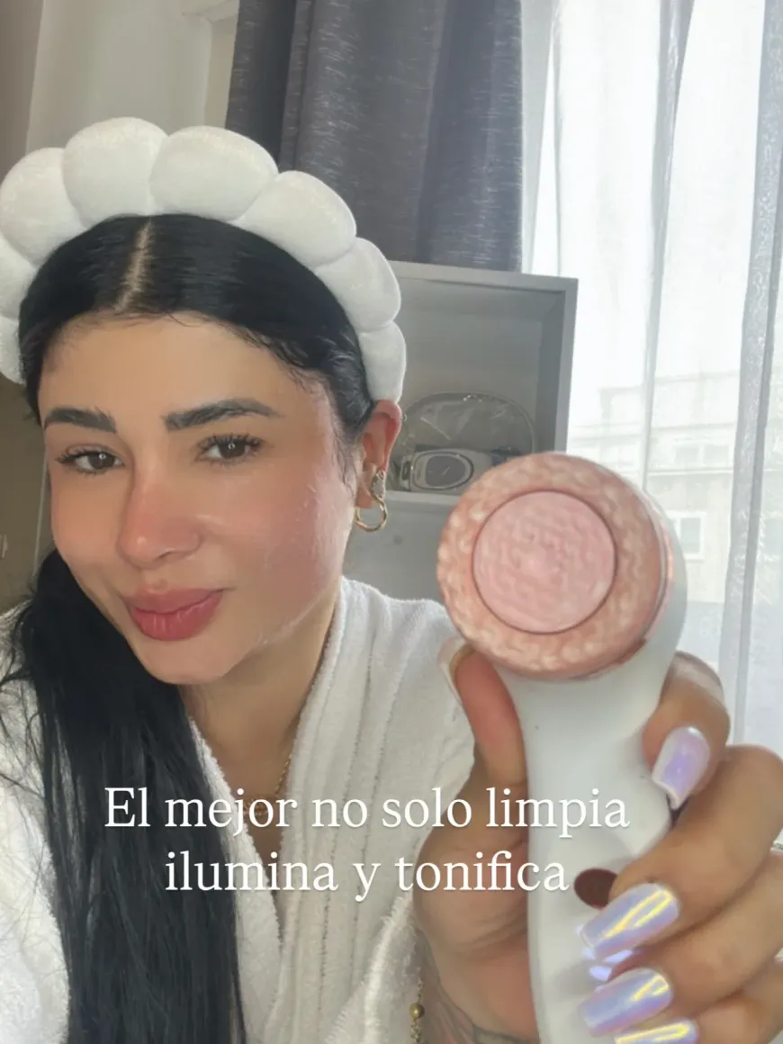 Mujer con diadema sosteniendo un dispositivo de limpieza facial rosa y blanco, texto en español.