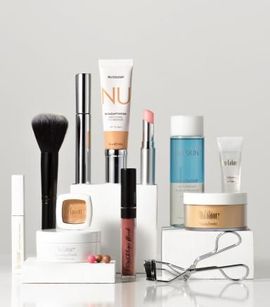 Cosméticos dispuestos en bloques blancos: pincel, rímel, base, labiales, polvos, maquillaje de ojos