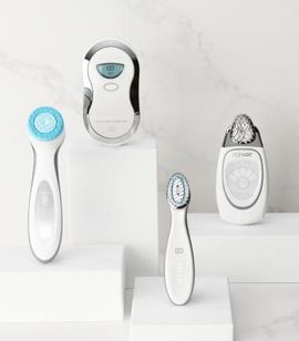 Cuatro dispositivos para el cuidado de la piel de color blanco y plateado sobre pedestales blancos sobre un fondo de mármol.