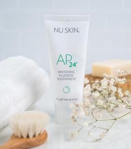 Tubo de pasta de dientes blanqueadora Nu Skin AP24 con flores, jabón y cepillo.