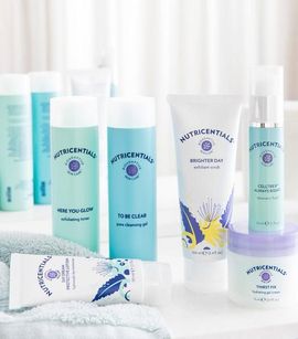 Productos para el cuidado de la piel sobre una superficie blanca, con botellas y tubos de color azul y blanco.