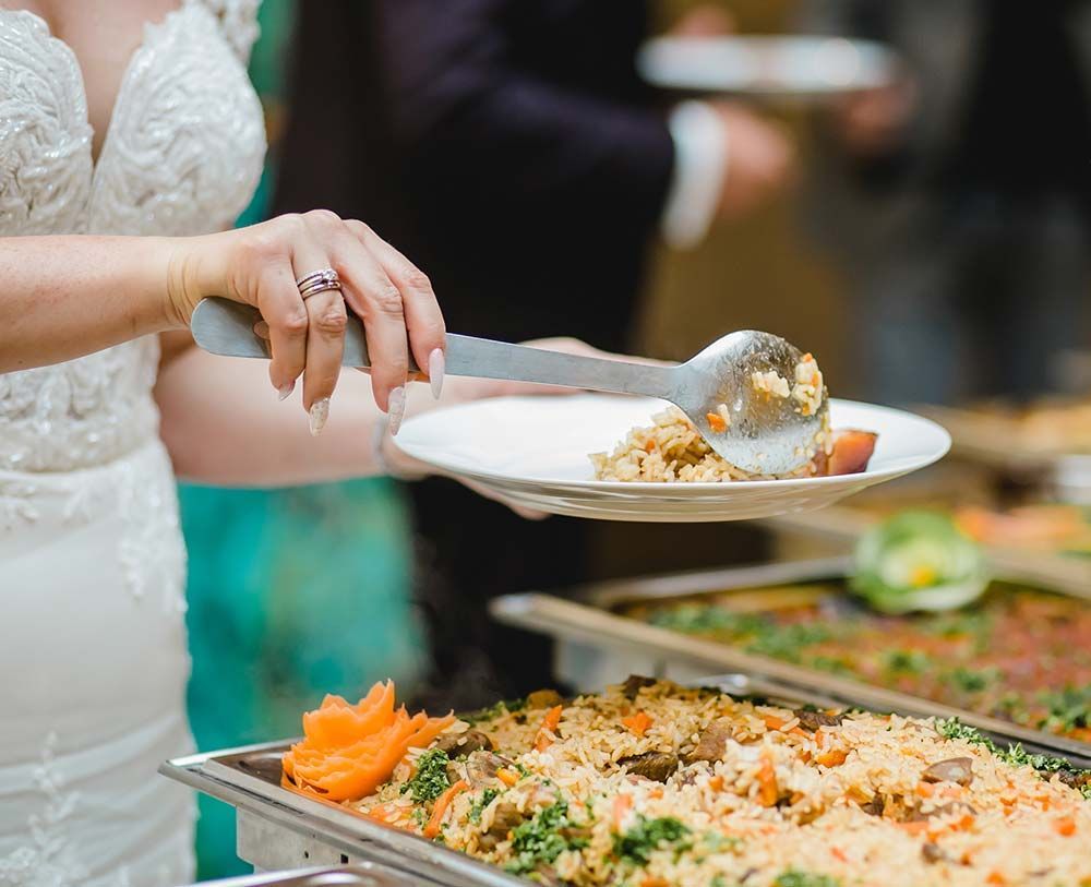 Una novia está sirviendo comida de un buffet en la recepción de su boda.