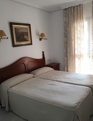 Dormitorio con dos camas individuales, cabecero de madera, obras de arte, ropa de cama beige y cortinas.