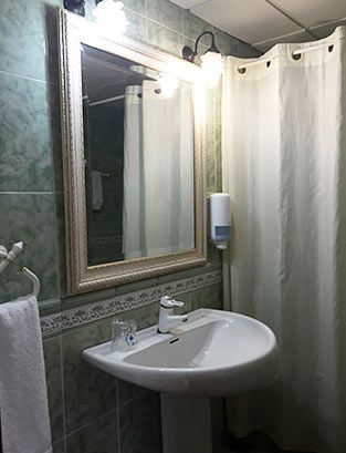 Baño con lavabo blanco, espejo, cortina de ducha y paredes de azulejos verdes.