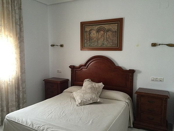 Dormitorio con cama, mesitas de noche, obras de arte y ventana con cortinas.