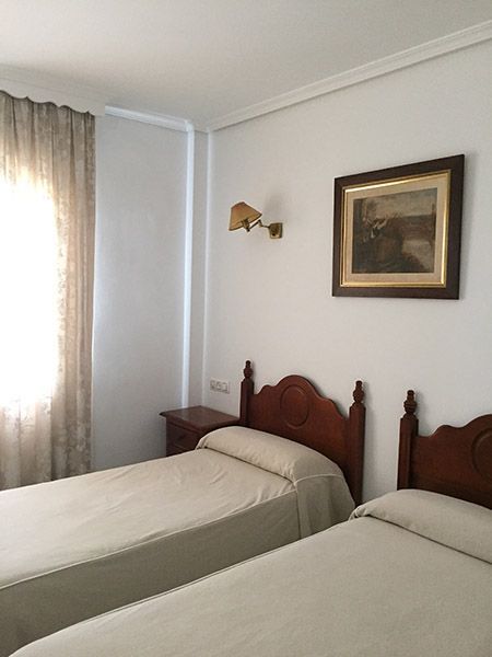 Dos camas individuales con cabeceros de madera en una habitación con ventana, cuadro y aplique.