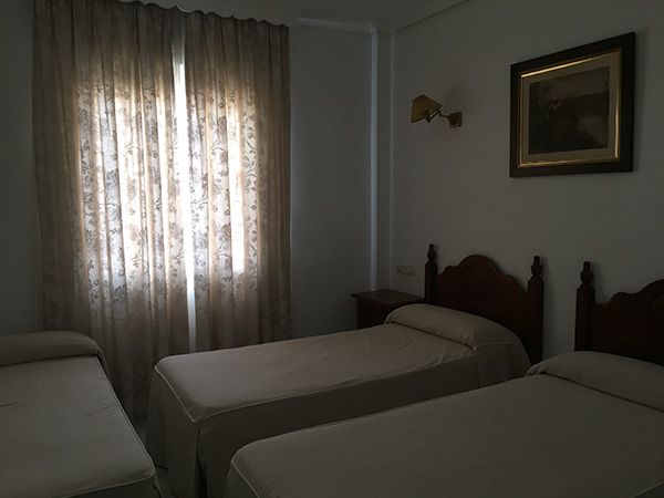 Tres camas en una habitación de hotel con ventana y arte enmarcado en la pared.