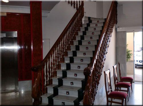 Escalera con pasamanos de madera, escalones en blanco y negro y detalles en rojo en la entrada de un edificio.