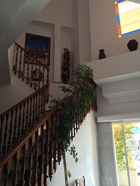 Escalera de madera con barandilla de color marrón oscuro; vegetación artificial; obra de arte en la pared; ventana de cristal.