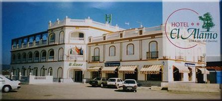 Edificio del Hotel El Álamo con coches aparcados en el frente, bajo un cielo azul.