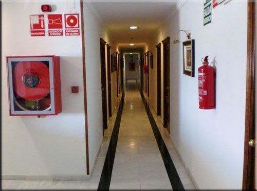 Pasillo de hotel con puertas, equipo de seguridad contra incendios y suelo de mármol.