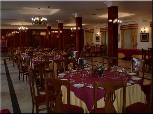Comedor formal con manteles rojos, mesas preparadas y candelabros ornamentados.