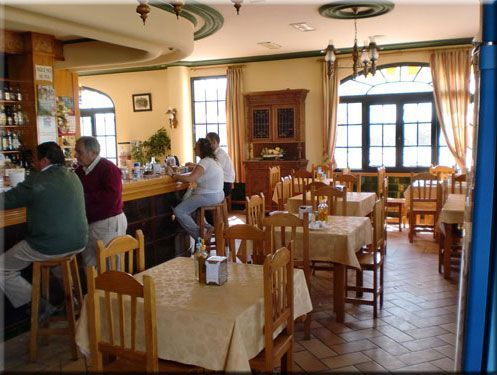 Interior de restaurante con barra y mesas. La gente está sentada en la barra y en las mesas. Sala luminosa y soleada.