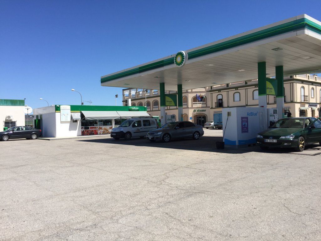 Gasolinera BP con marquesina verde y blanca y algunos coches aparcados cerca de los surtidores en un día soleado.