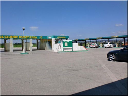 Un lavadero de coches con plazas cubiertas y coches, bajo un cielo despejado.