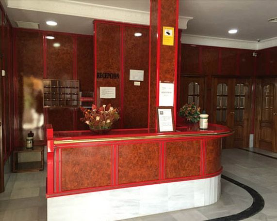Mostrador de recepción de hotel con detalles en rojo y paneles de madera oscura.