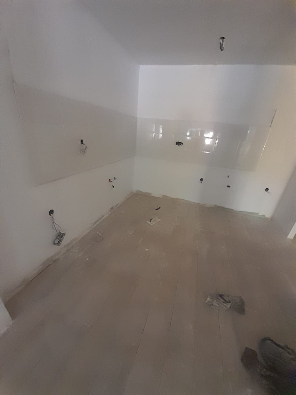 Cocina vacía con paredes blancas, cableado expuesto y piso sin terminar.