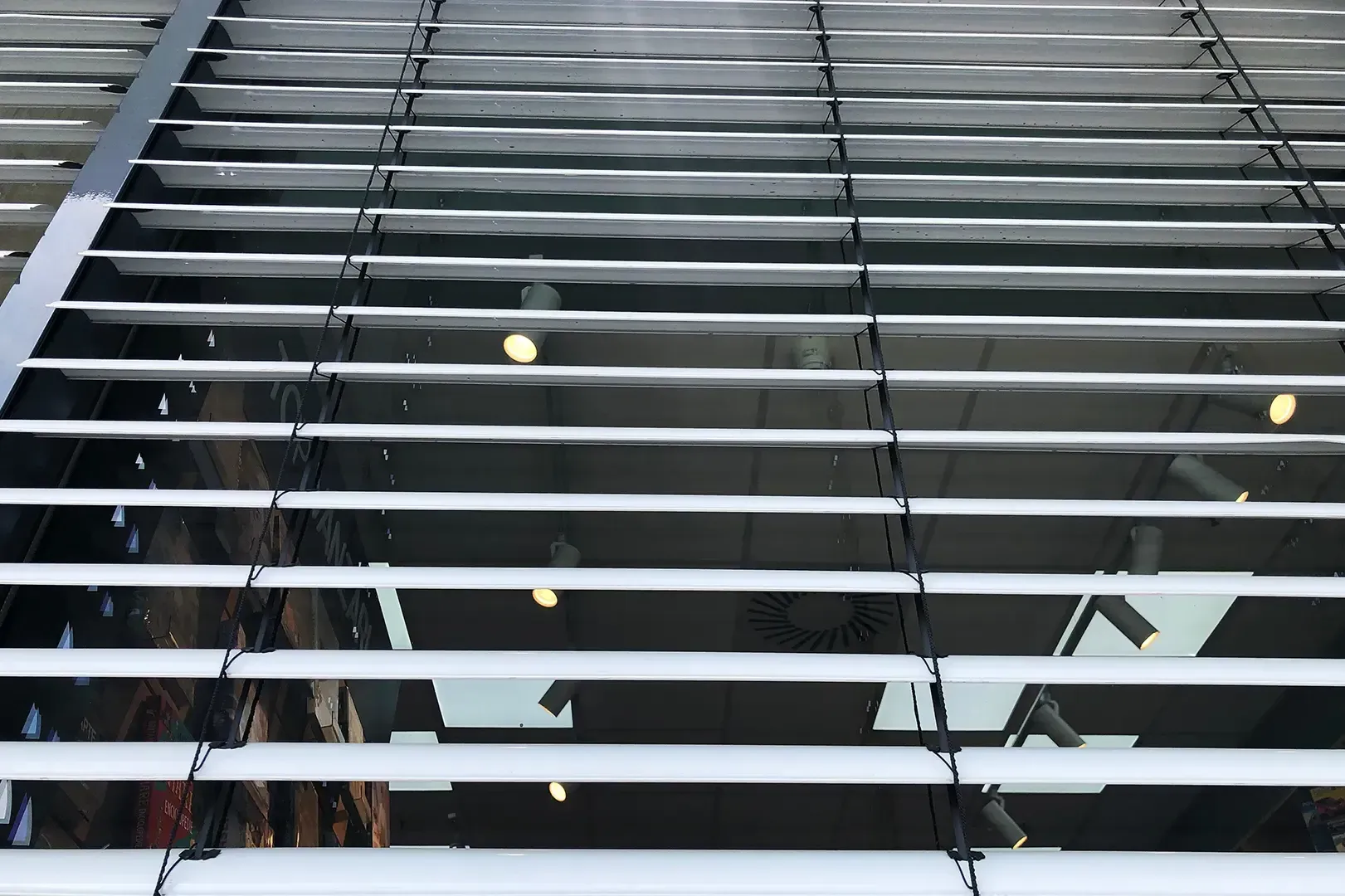 Die horizontalen Jalousien sind teilweise geöffnet und geben den Blick auf einen dunklen Innenraum mit eingeschalteter Deckenbeleuchtung frei.