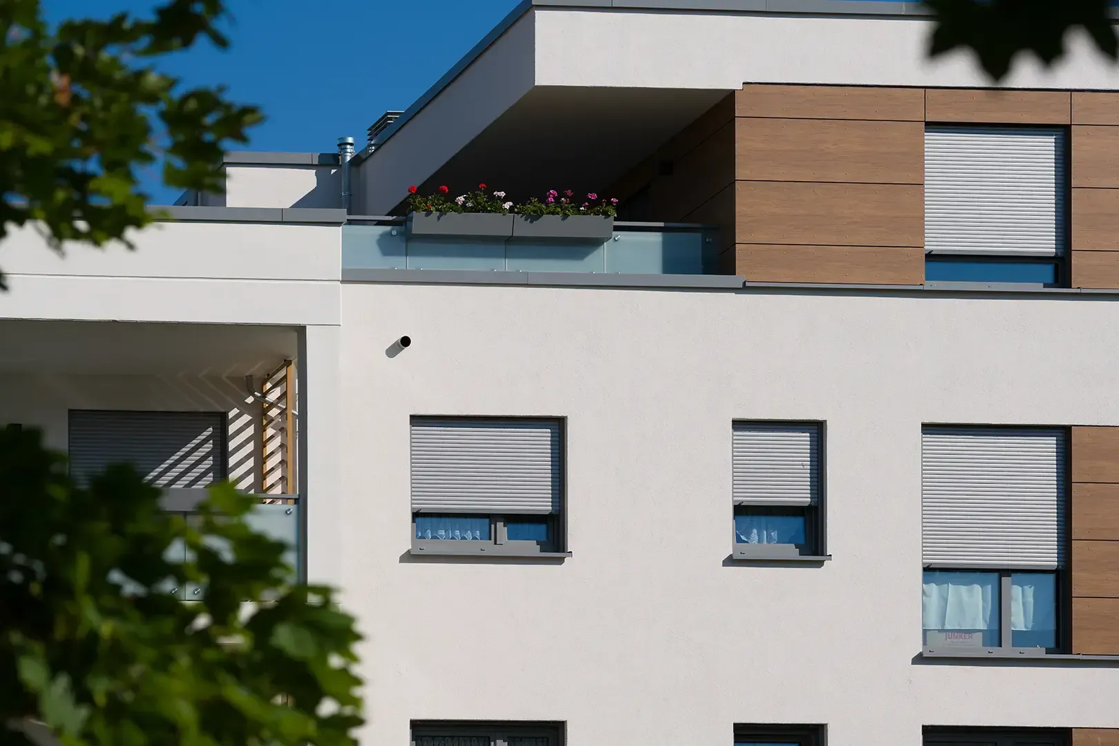 Ein modernes, weißes mehrstöckiges Wohngebäude mit holzvertäfelten Akzenten, Balkonen und beschatteten Fenstern.