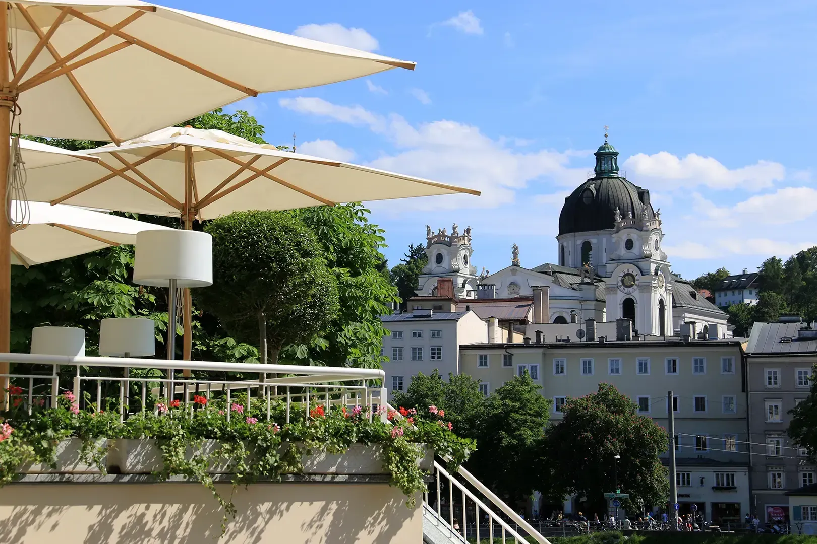 Sitzplätze im Freien unter weißen Sonnenschirmen mit Blick auf die Kuppel und die historische Architektur Salzburgs, Österreich.