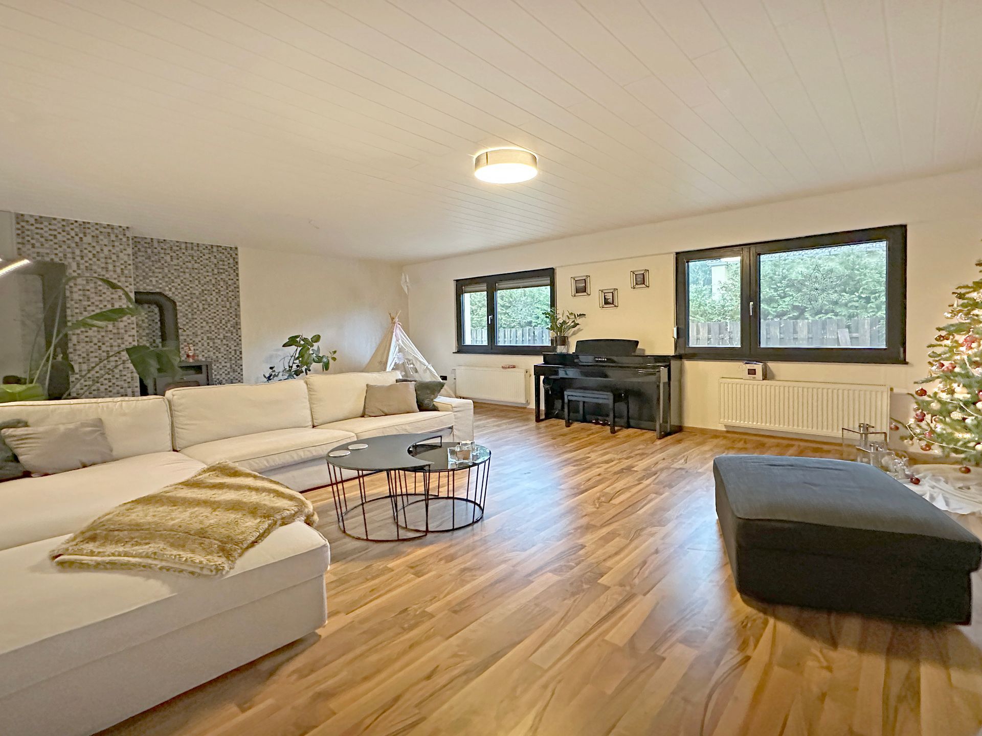 Ein Wohnzimmer mit Hartholzböden, einer Couch, einem Klavier und einem Weihnachtsbaum.