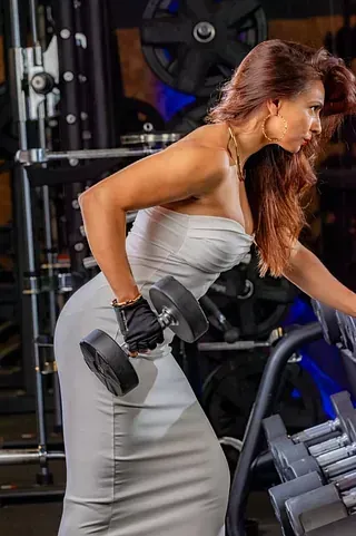 Una mujer con un vestido blanco está levantando una mancuerna en un gimnasio.