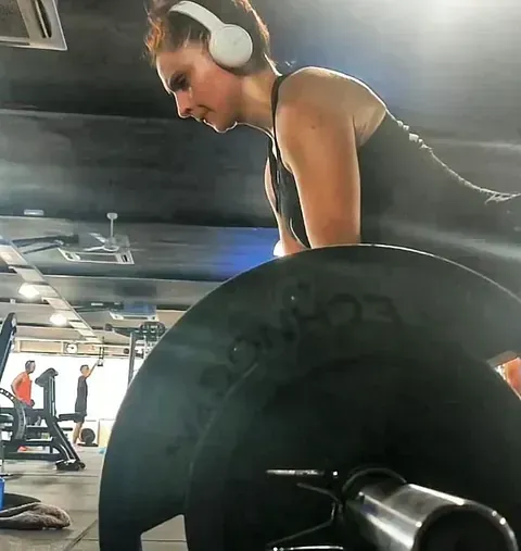Una mujer con auriculares está levantando pesas en un gimnasio.