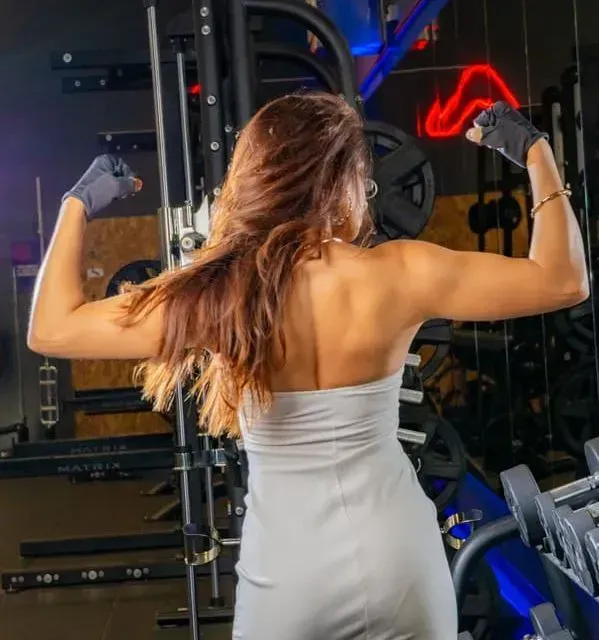 Una mujer con un vestido blanco está flexionando sus músculos en un gimnasio.