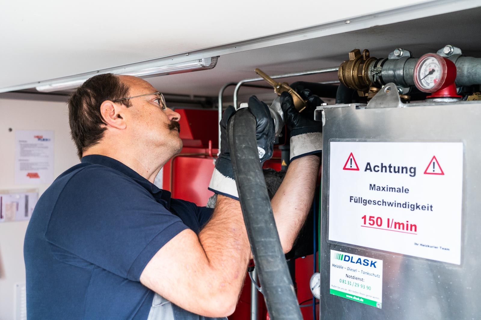 Ein Arbeiter schließt einen dicken Schlauch an einen Tank mit Warnhinweis „Maximale Füllgeschwindigkeit 150 l/min“ an.