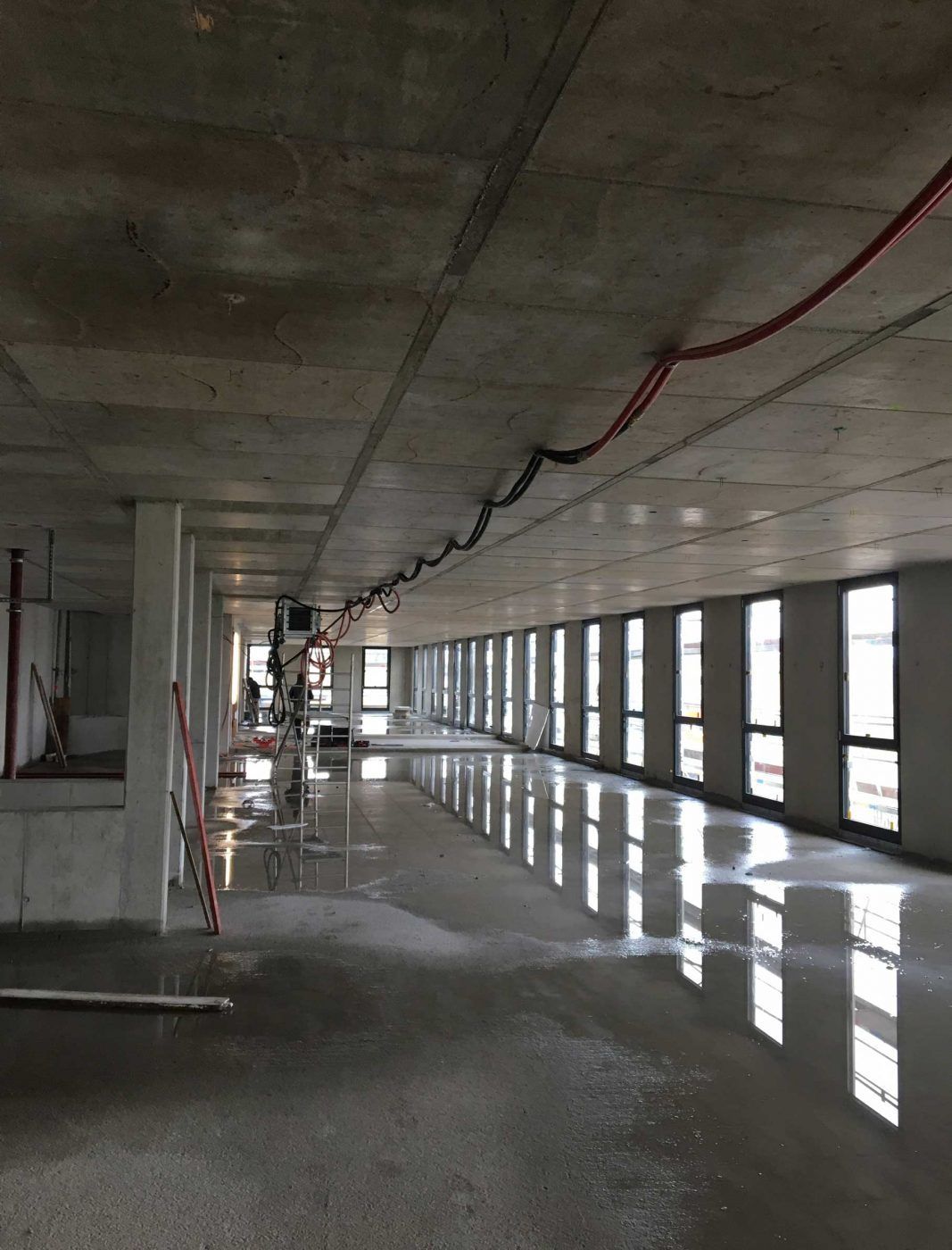 Ein Rohbau mit Betonboden, auf dem sich Wasser gesammelt hat, und Kabeln, die unter der Decke hängen.