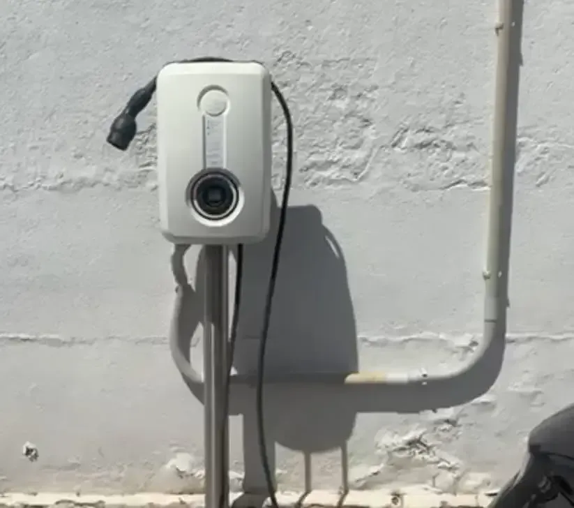 Caja blanca para cámara de seguridad montada en la pared sobre una pared exterior gris con conductos y cables.